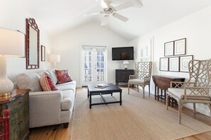 A living room with a sofa, coffee table, and chairs, a television, and a ceiling fan.