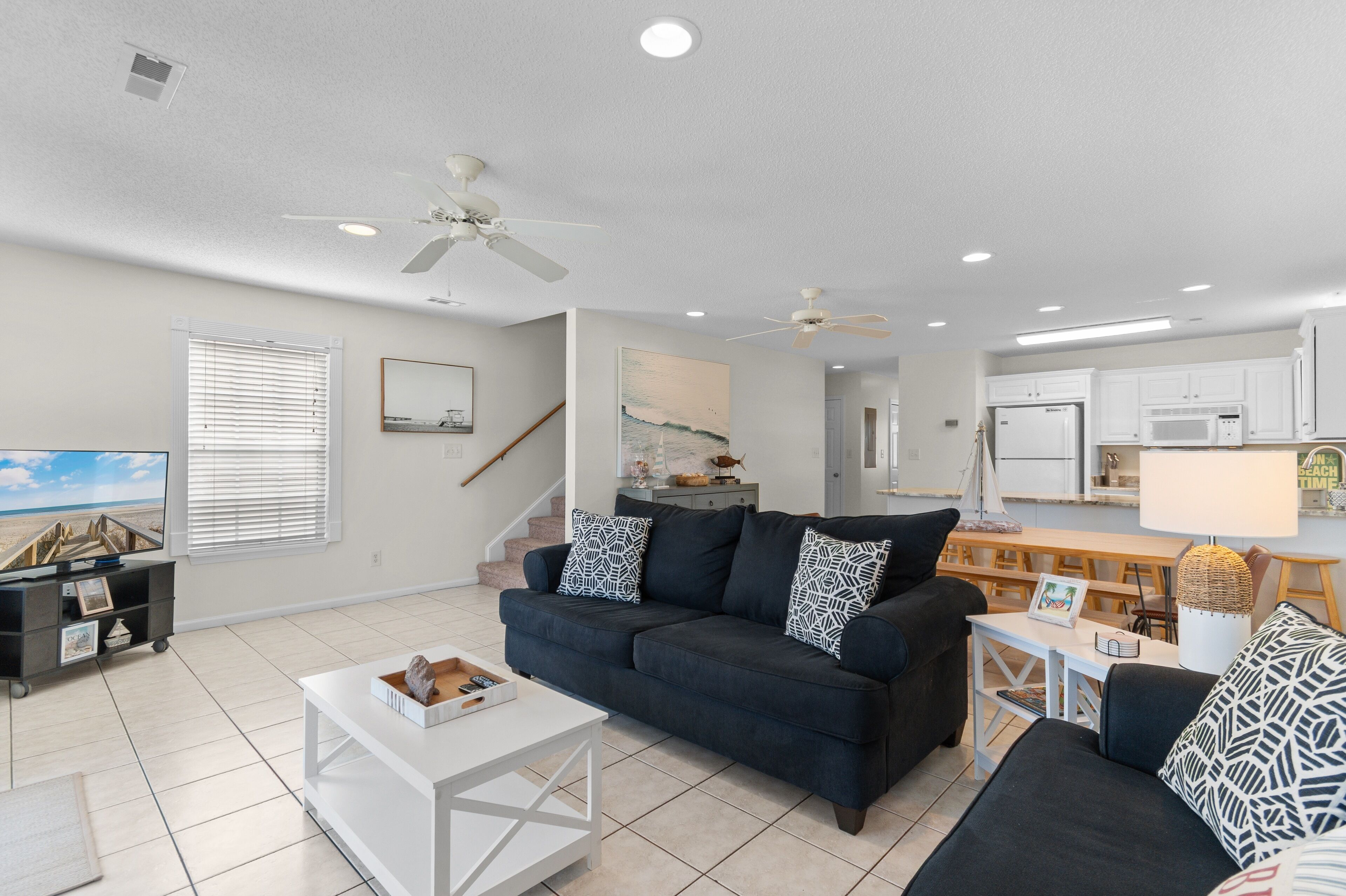 A modern living room with a dark blue sofa, white coffee table, and a staircase leading to an upper level.