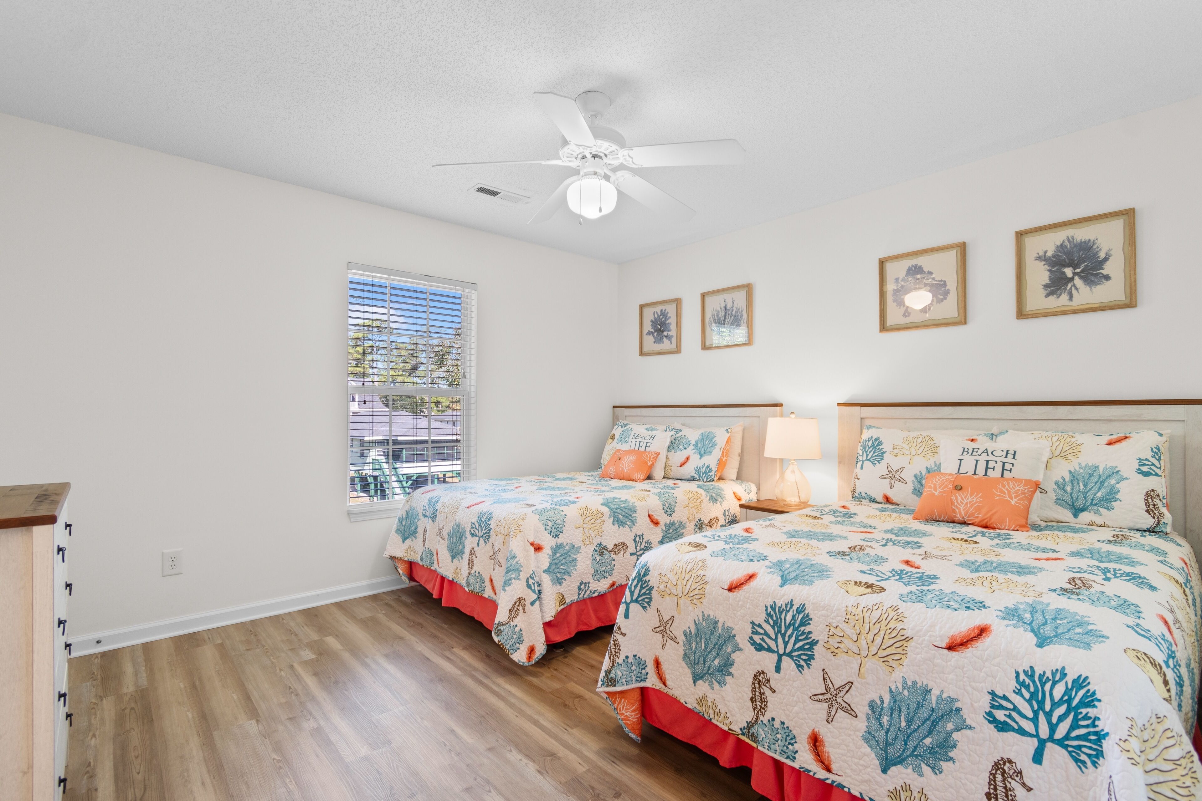 A bedroom with two beds, a ceiling fan, and a window with blinds.