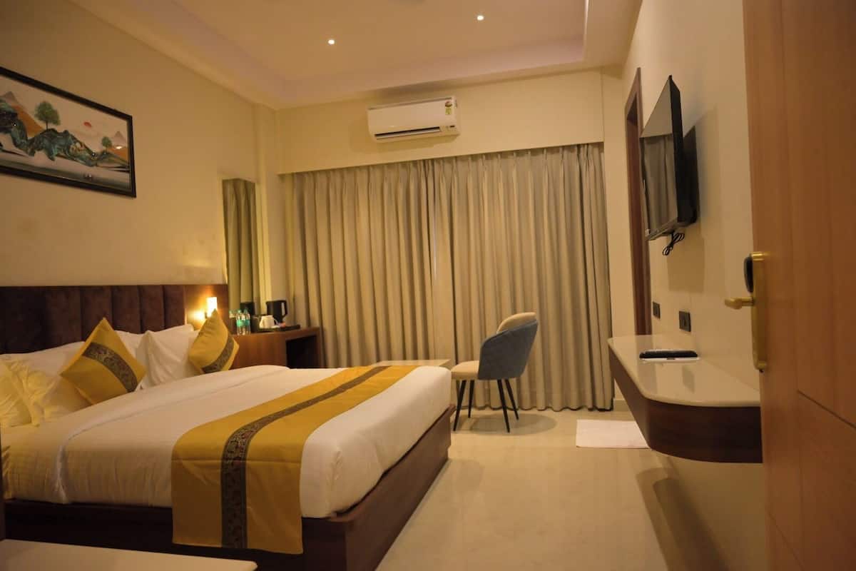 A hotel room with a large bed, a desk, a chair, an air conditioning unit, a television, and a painting on the wall.