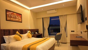 Ein Hotelzimmer mit einem großen Bett, einem Schreibtisch, einem Stuhl, einem Fernseher und einem Vorhangfenster.
