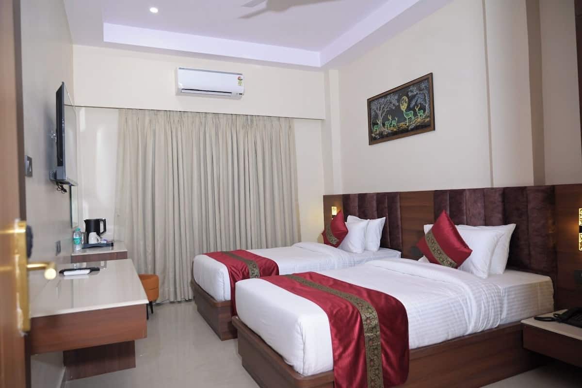 A hotel room with two beds, a desk, a coffee maker, an air conditioner, and a painting on the wall.