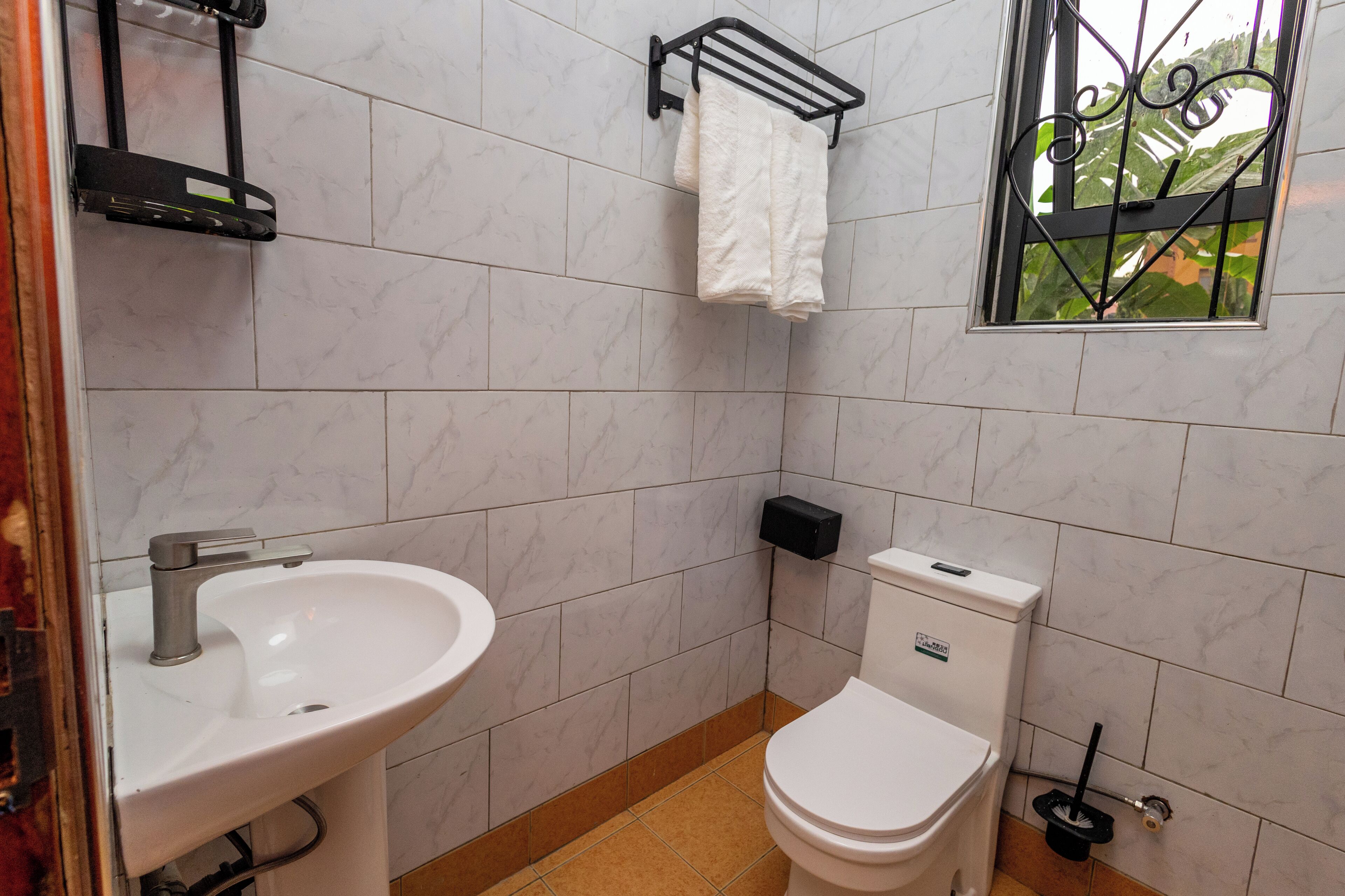 Casa de banho com lavatório branco, sanita e janela com grades de metal.