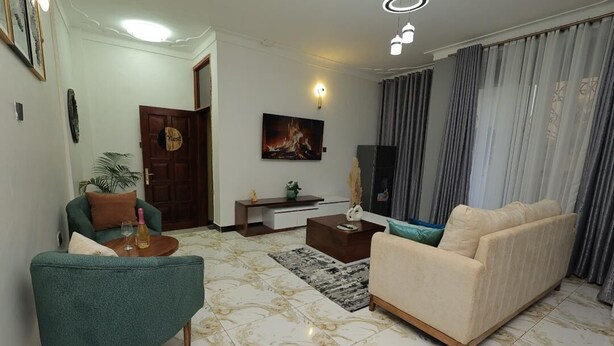 A living room with a sofa, armchair, coffee table, and a painting on the wall. - The Nest Kampala (Kampala)