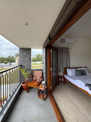 A balcony with a wooden chair, a small table with a vase and a plant, and a bed with pillows. - Breezy villa (Shrirangapattana)