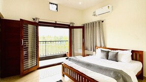 A bedroom with a bed, a ceiling fan, an air conditioning unit, a balcony with a view, and a patterned rug. - Breezy villa (Shrirangapattana)