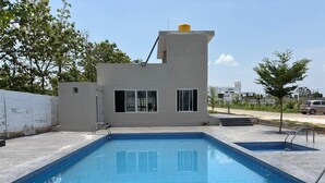 A rectangular swimming pool with a tiled edge, surrounded by a paved deck. - Breezy villa (Shrirangapattana)