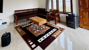 A living room with a sofa, chairs, a coffee table, a ceiling fan, a window with curtains, and a door. - Breezy villa (Shrirangapattana)