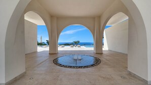 Un'area esterna coperta con una fontana circolare, archi e vista sul mare.