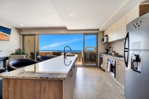 A modern kitchen with a central island, stainless steel appliances, and a view to the outside. - Stunning Brand New Condo - Pool & Ocean Views (Cabos San Lucas)