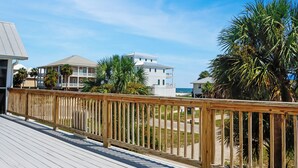 A wooden deck with a railing, palm trees, and buildings in the background. - ☀️Short, 3 Min Walk to Beach | Gulf Views | Papa's Palmetto Place☀️ (Indian Pass)