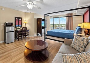 A hotel room with a bed, a dining area, a kitchenette, a round table, and a view of the outdoors.