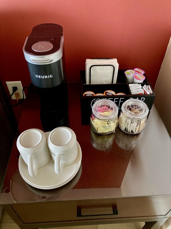 A coffee maker, two cups, a napkin holder, and a box of coffee pods on a table.
