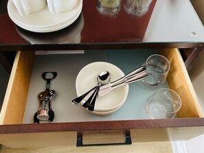A drawer with a white plate, a spoon, a glass, and a bottle opener.