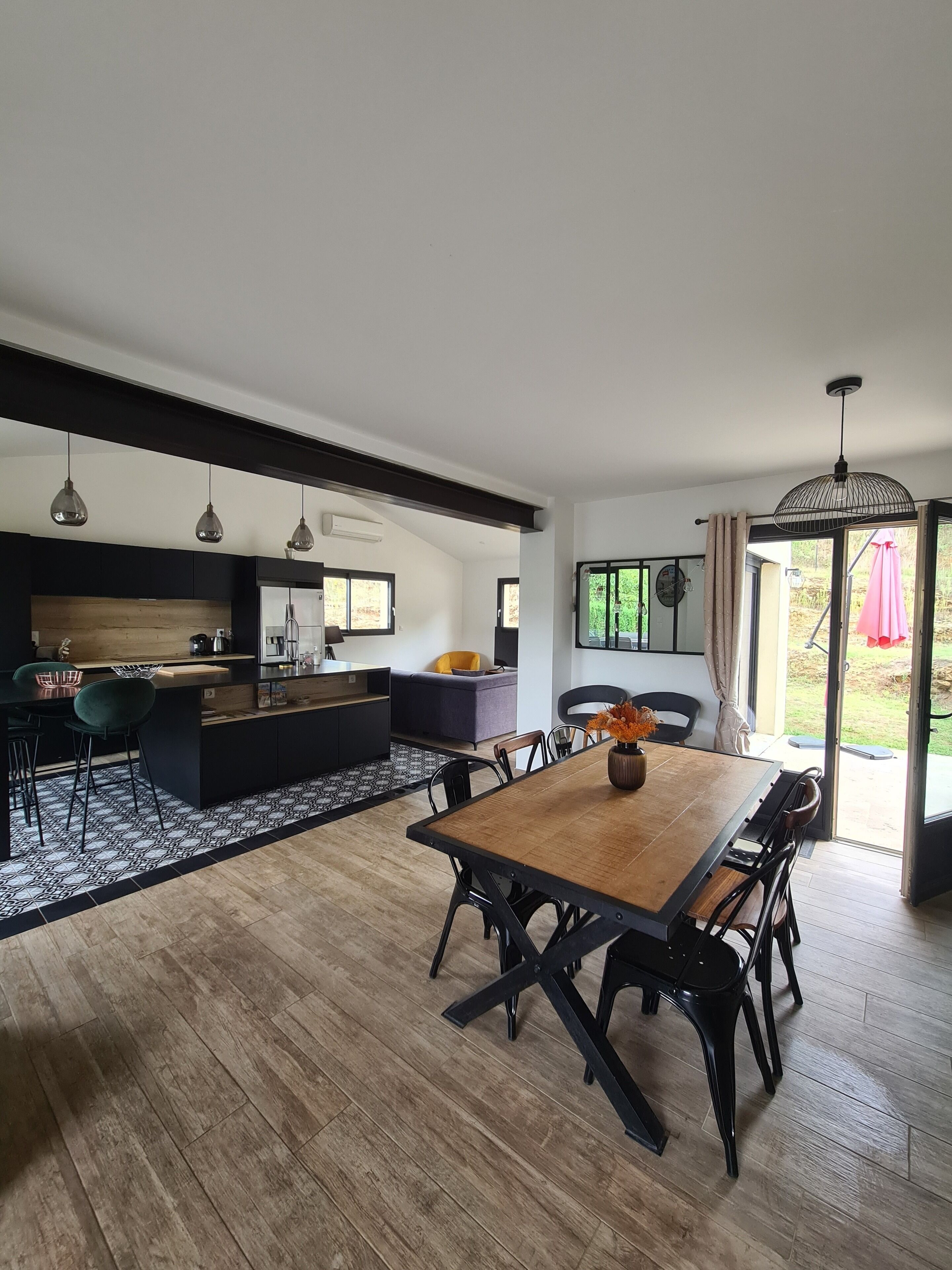 Une cuisine moderne avec des meubles de couleur sombre, un îlot central en bois et des luminaires suspendus.