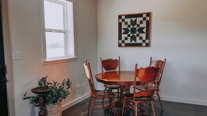 Uma sala de jantar com mesa e cadeiras de madeira, uma planta em vaso e um tabuleiro de xadrez na parede.