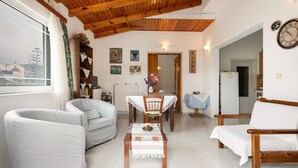 Una sala de estar con una mesa de comedor, dos sofás, techo de madera y vista a un edificio.