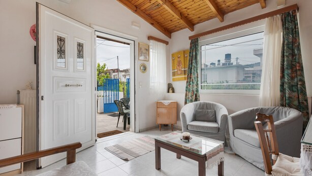 Una sala de estar con techo de madera, una puerta blanca, una mesa de centro de vidrio y dos sofás.