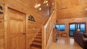 A wooden interior with a staircase, wooden walls, and large windows offering a view. - Forever View- Mountain View Cabin (Blue Ridge)