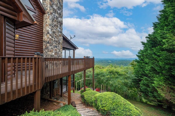 A wooden cabin with a stone exterior, a balcony, and a view of the forest.