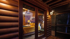 A log cabin with a wooden deck, a bed with a yellow bedspread, and a window with a view of the outdoors. - Forever View- Mountain View Cabin (Blue Ridge)