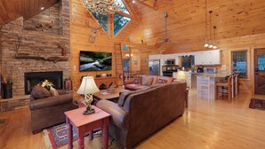 A spacious living room with a fireplace, a large sofa, and a dining area with a kitchen in the background. - Forever View- Mountain View Cabin (Blue Ridge)