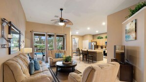 A spacious living room with a ceiling fan, a dining area with chairs, a kitchen with cabinets, and a large window offering a view of the outdoors. - FP8104 Windsor Palms Resort Vacation Home (Kissimmee)