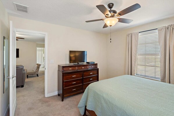 Une chambre à coucher comprenant un lit, une commode, un ventilateur de plafond et un téléviseur.