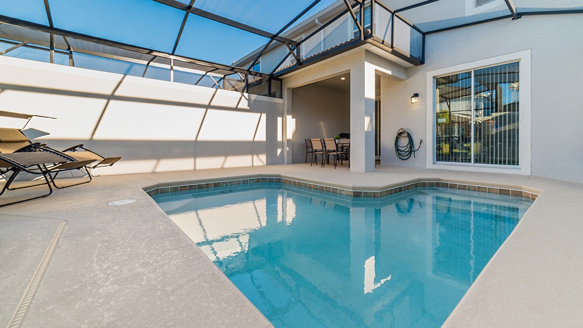 An indoor swimming pool with a glass ceiling, lounge chairs, and a table with chairs.
