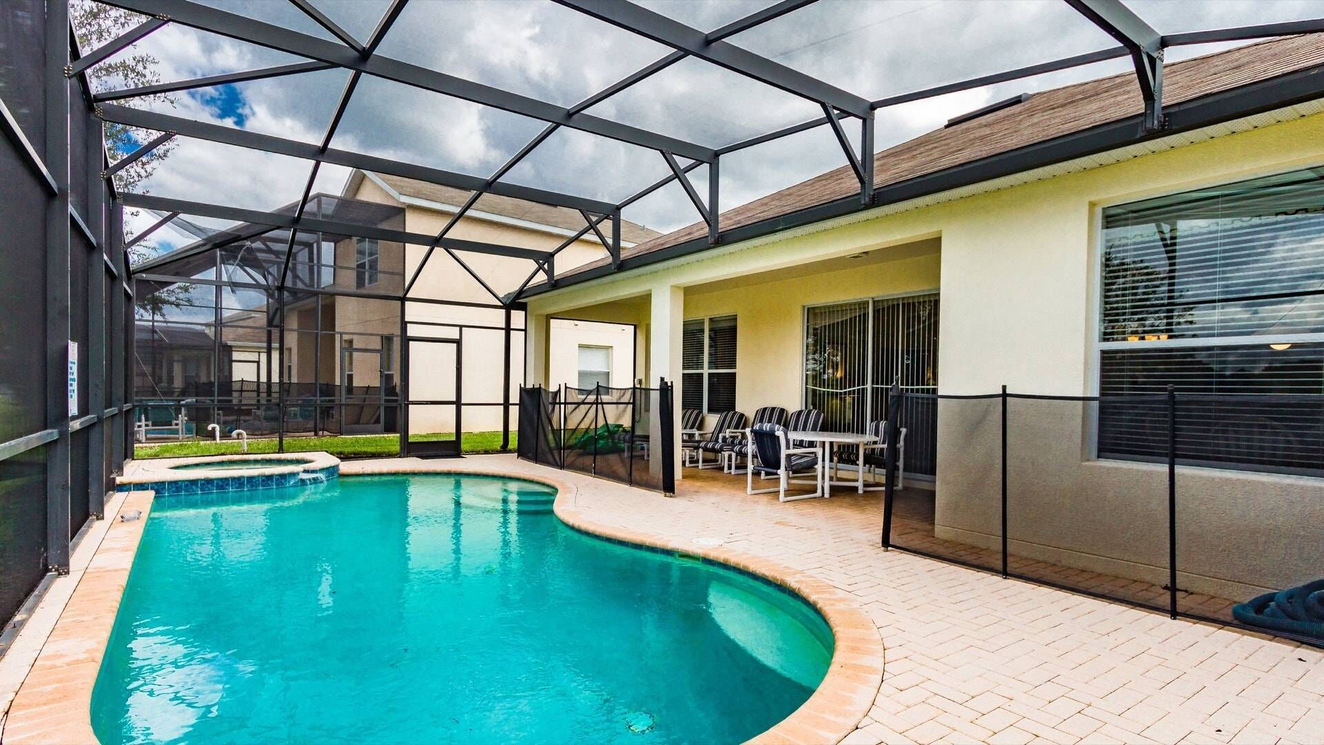A swimming pool with a glass enclosure, a patio area with chairs, and a covered seating area.