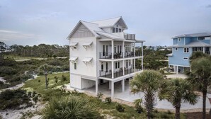 A two-story house with a balcony on the upper floor, surrounded by a natural landscape with trees and shrubs. - Cape San Blas Gem w/ Sunrise + Sunset Views (Port St Joe)