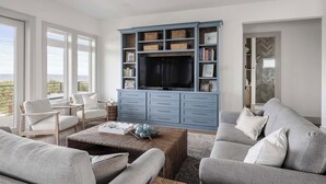A living room with a large TV, comfortable seating, and a view through the windows. - Cape San Blas Gem w/ Sunrise + Sunset Views (Port St Joe)