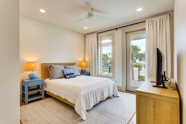 A bedroom with a bed, nightstands, a TV, and a view of the outdoors. - Cape San Blas Gem w/ Sunrise + Sunset Views (Port St Joe)