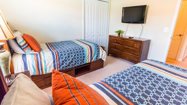 A bedroom with two beds, a dresser, a television, and a door.