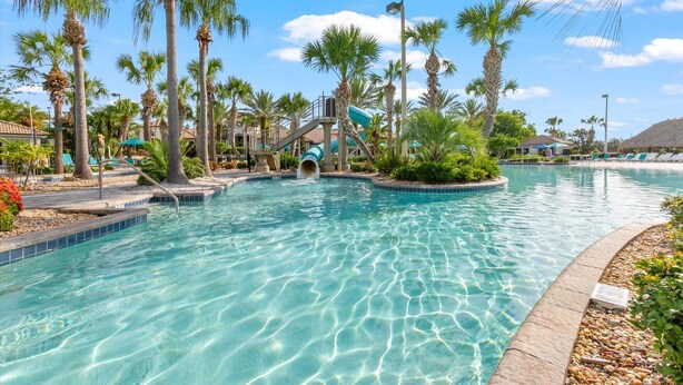 A clear pool with palm trees, a water slide, and lounge chairs. - Cdw9161 (Four Corners)