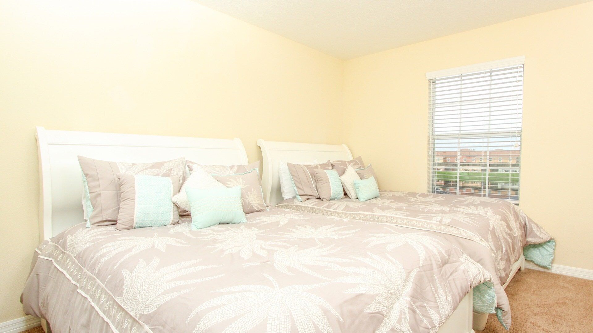 A bedroom with two beds, beige walls, and a window with blinds.