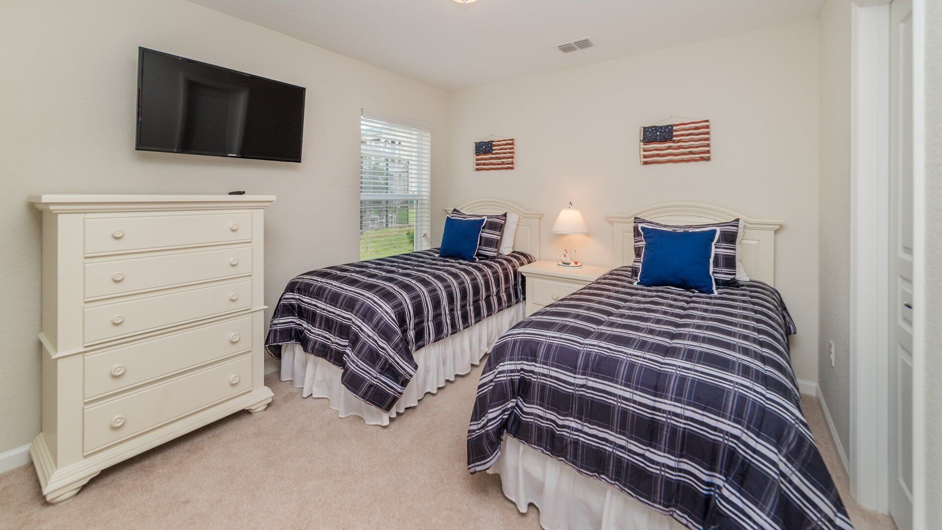 Une chambre avec deux lits, une commode, une télévision et des drapeaux américains accrochés au mur.