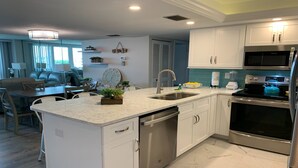 A modern kitchen with white cabinetry, stainless steel appliances, and a marble countertop.