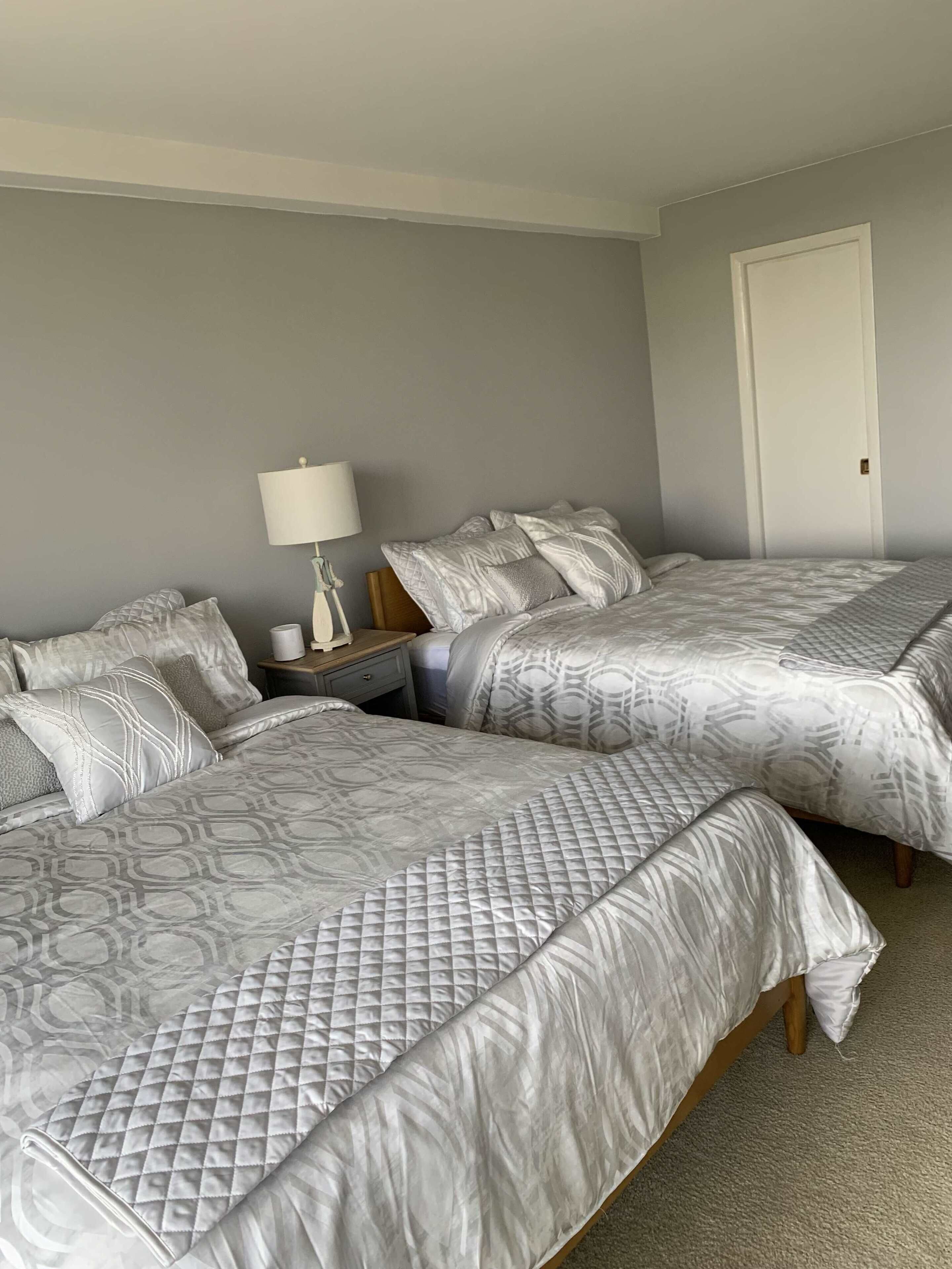 A bedroom with two beds, a nightstand, a lamp, and a door.