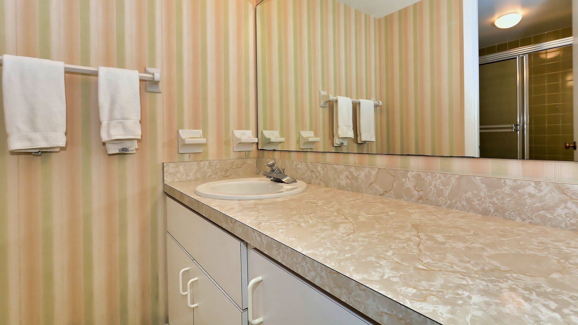 Un bany amb paper pintat a ratlles, un lavabo i un mirall.