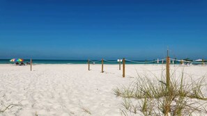 A beach with a volleyball net, a colorful umbrella, and a clear blue sky.