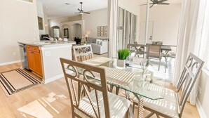 A spacious kitchen with a central island, a dining area with glass tables and chairs, and a view of the living room through a glass door. - Windsor Palms Resort Vacation Home WP2209 (Kissimmee)