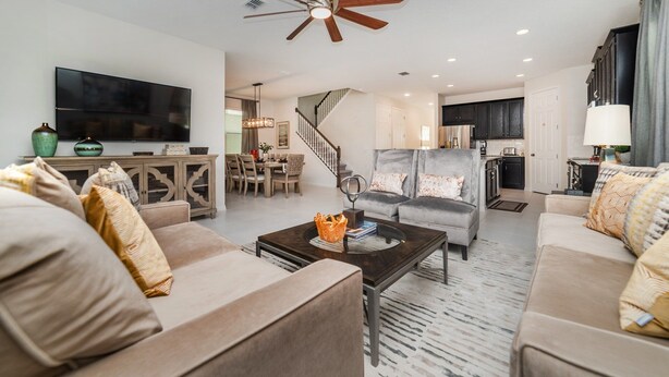 A spacious living room with a large flat-screen TV, a grey sofa, a coffee table, and a dining area with a staircase. - Solara Resort Vacation Home 5BR (Kissimmee)