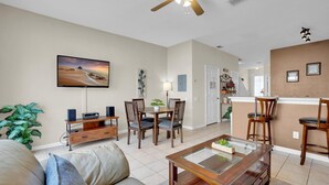 A living room with a TV, a coffee table, and a sofa. There is a dining area with chairs and a table. - Windsor Palms Resort Vacation Townhome 3BR (Kissimmee)