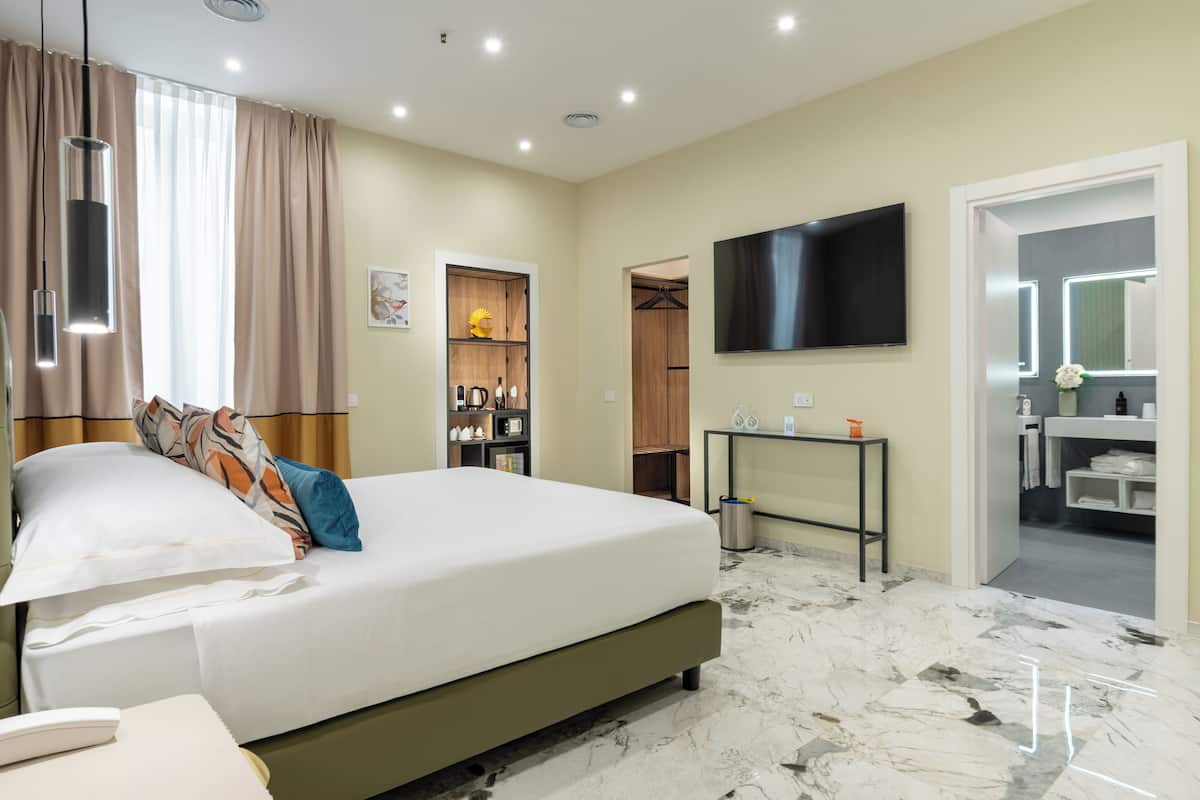 A hotel room with a bed, a TV, a vanity with a mirror, and a bathroom visible through an open door.