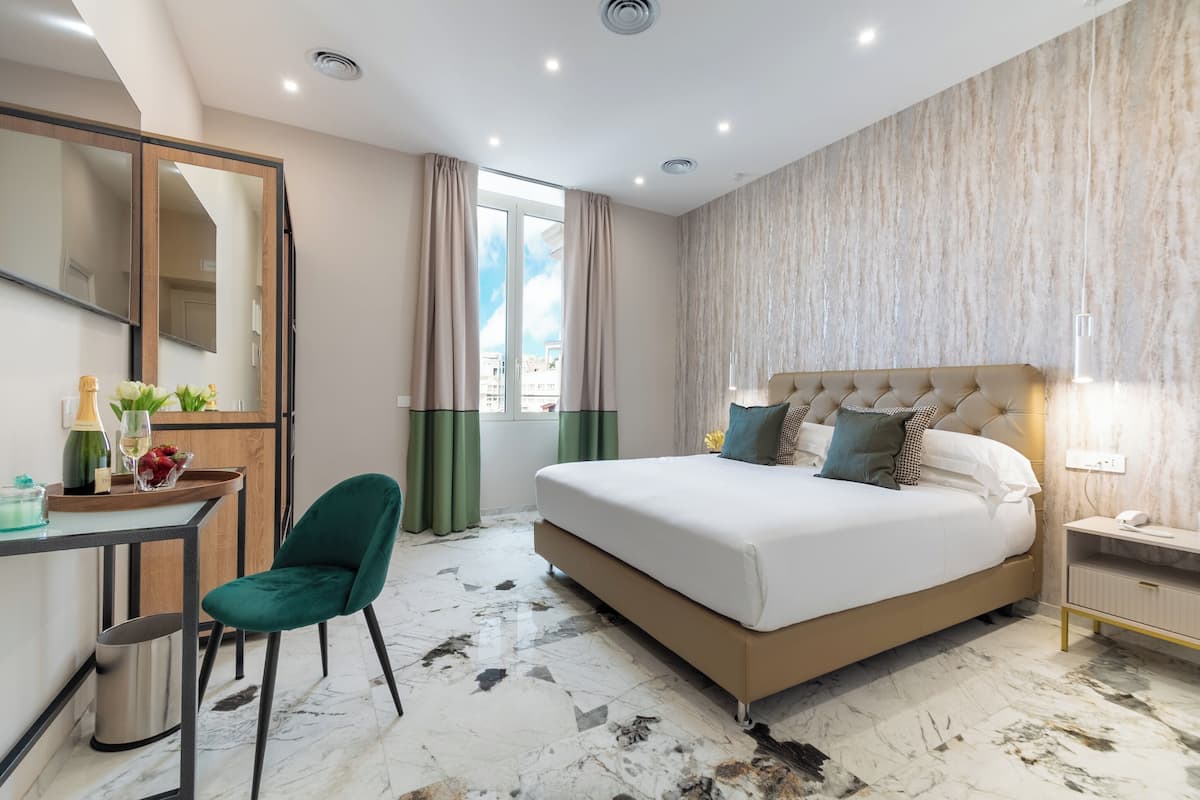 A modern hotel room with a bed, a desk, a chair, a mirror, and a window with curtains.