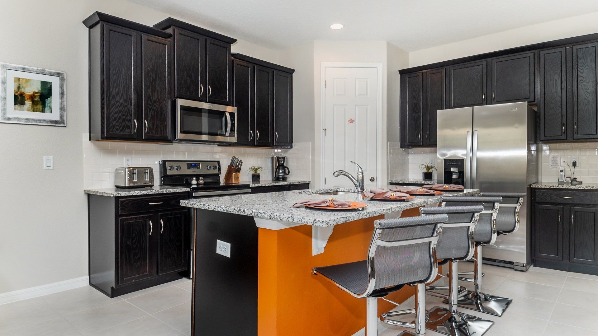 A modern kitchen with dark cabinetry, stainless steel appliances, and a central island with bar stools.
