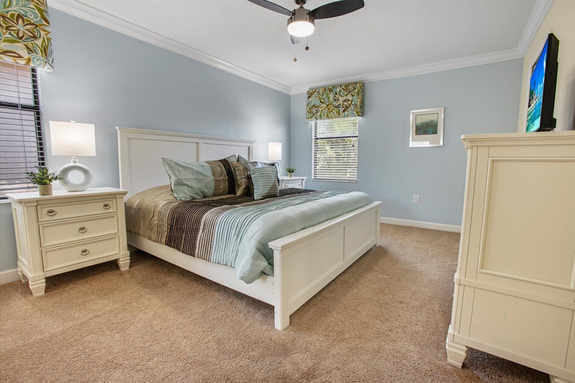 A bedroom with a bed, nightstands, a dresser, a ceiling fan, and a window with blinds.