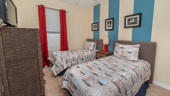 A bedroom with two beds, a TV, and a window with red curtains.
