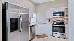 Une cuisine moderne dotée d’appareils électroménagers en acier inoxydable, de meubles blancs, d’un pare-feu en carreaux et d’un four encastré.